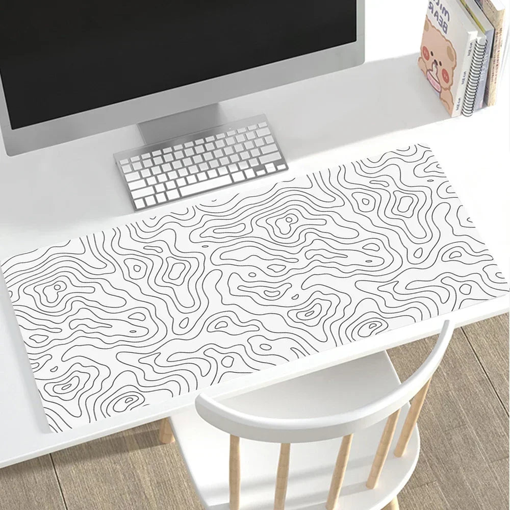 Desk setup with a computer, keyboard, and a large desk mat featuring a black and white topographic pattern.