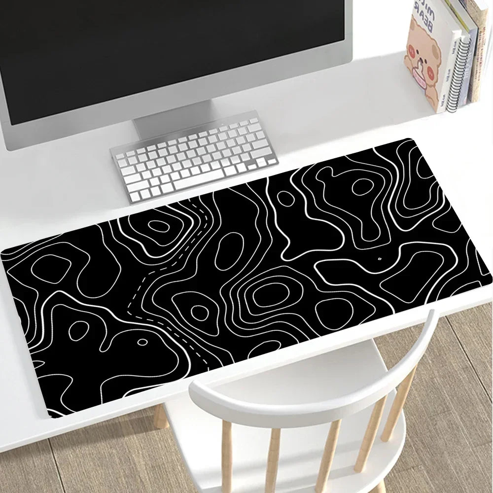 Large desk mat with black background and white pattern on a white desk with white chair and computer monitor. 